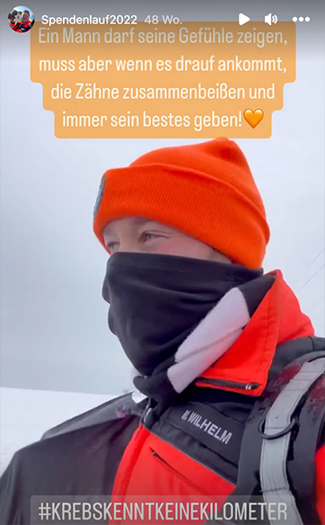 Ein Screenshot aus einer Instagram-Story von Marcel Wilhelm. Auf dem Bild ist er zu sehen, wie er in kompletter Ausrüstung des Rettungsdienstes durch eine verschneite Landschaft läuft. In einer Textblase oben steht der Text "Ein Mann darf seine Gefühle zeigen, muss aber wenn es darauf ankommt, die Zähne zusammenbeißen und immer sein bestes geben!". Unten steht außerdem #krebskenntkeinekilometer