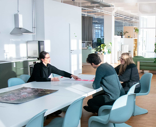 Drei Kolleginnen und Kollegen sitzen zusammen an einem Konferenztisch und betrachten ein Flipchart, das auf dem Tisch liegt.